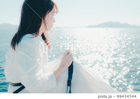 浜辺に佇むカメラを持った若い女性の写真 99434544