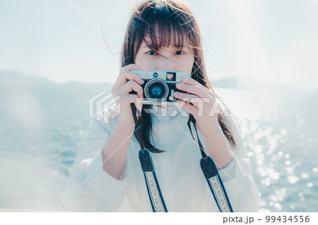 浜辺に佇むカメラを持った若い女性の写真 浜辺に佇むカメラを持った若い女性の写真 99434556