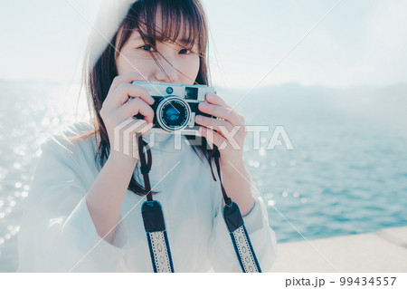 浜辺に佇むカメラを持った若い女性の写真 浜辺に佇むカメラを持った若い女性の写真 99434557