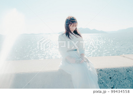 浜辺に佇むカメラを持った若い女性の写真 浜辺に佇むカメラを持った若い女性の写真 99434558