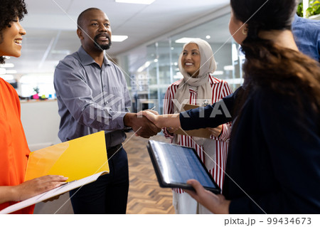 Happy diverse female and male businesspeople talking and shaking hands in office 99434673