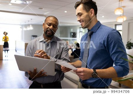 Image of diverse male colleagues working and talking in office 99434706