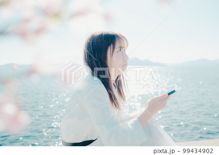 浜辺に佇み音楽を聴く若い女性の写真 99434902