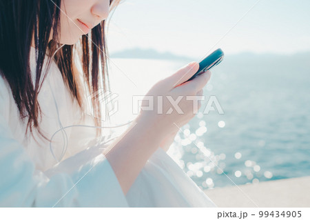 浜辺に佇み音楽を聴く若い女性の写真 99434905