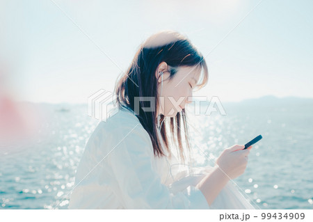 浜辺に佇み音楽を聴く若い女性の写真 99434909