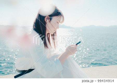 浜辺に佇み音楽を聴く若い女性の写真 99434914