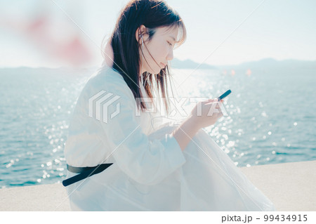 浜辺に佇み音楽を聴く若い女性の写真 99434915