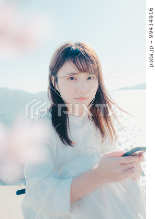 浜辺に佇み音楽を聴く若い女性の写真 99434916