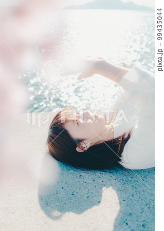 浜辺に佇み音楽を聴く若い女性の写真 99435044