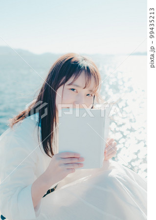 浜辺に佇み本を持っている若い女性の写真 99435213
