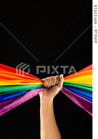 Hand holding rainbow coloured flag with copy space on black background 99435618