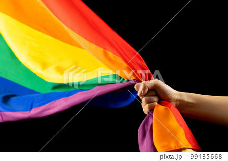 Hand holding rainbow coloured flag with copy space on black background Hand holding rainbow coloured flag with copy space on black background 99435668