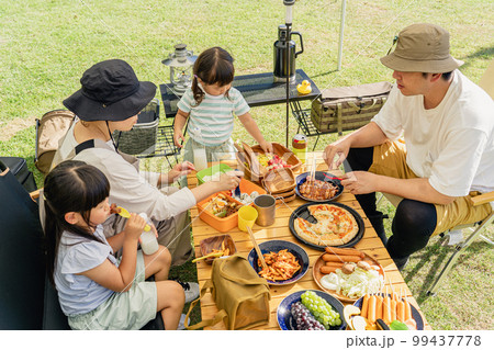 キャンプ場でバーベキュー・キャンプ飯を食べる家族（アウトドア・旅行・レジャー・ピクニック） 99437778
