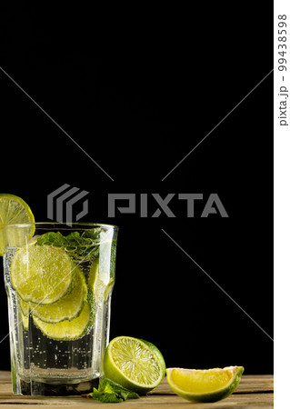 Glass with water and limes on wooden table with copy space over black background Glass with water and limes on wooden table with copy space over black background 99438598
