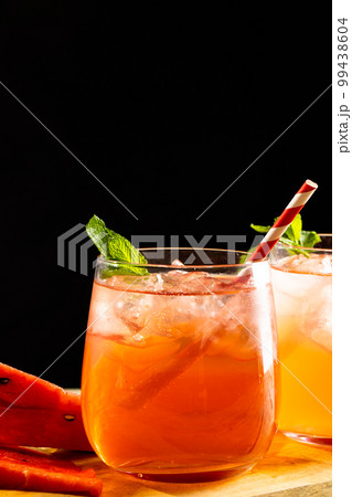 Glasses with cocktail and straws on wooden board with copy space over black background 99438604