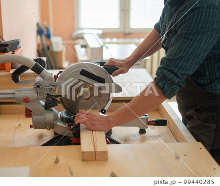 Master cuts the board with a circular saw in the workshop. Master cuts the board with a circular saw in the workshop. 99440285