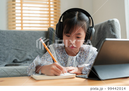 Asian little girl doing homework, using digital tablet with headphone. Asian little girl doing homework, using digital tablet with headphone. 99442014