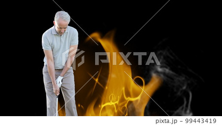Caucasian senior male golf player holding club against fire flame effect on black background Caucasian senior male golf player holding club against fire flame effect on black background 99443419