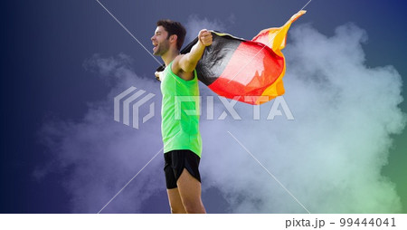Composition of strong smiling caucasian male athlete holding german flag on blue background 99444041