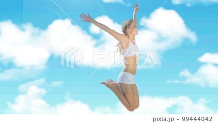 Composition of fit smiling woman in white underwear jumping over clouds on blue sky 99444042