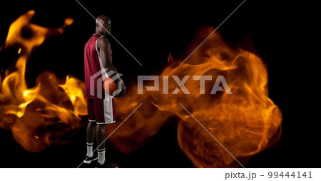 Composition of male basketball player standing holding ball over flames on black background Composition of male basketball player standing holding ball over flames on black background 99444141