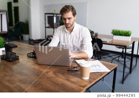 young businessman man in a white shirt works on laptops in the office young businessman man in a white shirt works on laptops in the office 99444295
