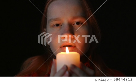 Young woman blowing out a candle on a black background 99444312