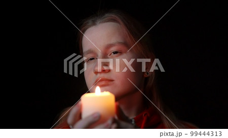 A girl with a candle in her hands is mysteriously examining something 99444313