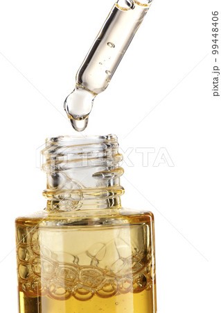 Part of a bottle with yellow cosmetic serum. Cosmetic glass pipette with a yellow oily drop of serum close-up on a white background. Part of a bottle with yellow cosmetic serum. Cosmetic glass pipette with a yellow oily drop of serum close-up on a white background. 99448406