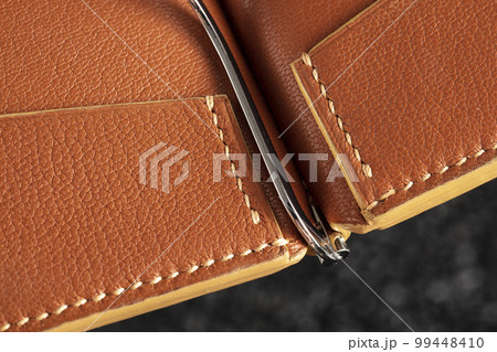 Part of a brown leather wallet or case with stitching. Part of a brown leather wallet or case with stitching. 99448410