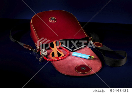 Red leather bag with women's accessories on a dark background. 99448481