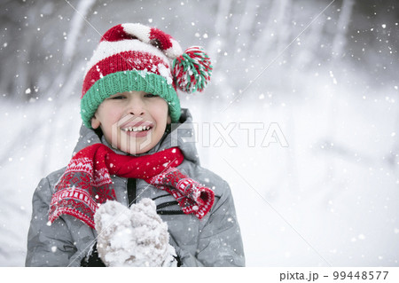 Happy boy on a winter day looks at the camera, smiles. A child plays in the winter with snow. Happy boy on a winter day looks at the camera, smiles. A child plays in the winter with snow. 99448577
