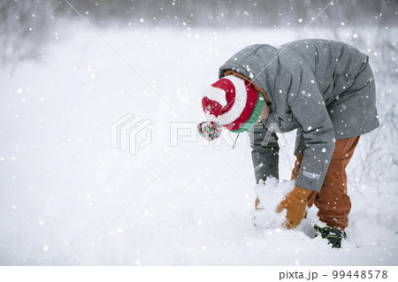 A boy makes a snowball on a snowy field. A child plays in the winter with snow. A boy makes a snowball on a snowy field. A child plays in the winter with snow. 99448578