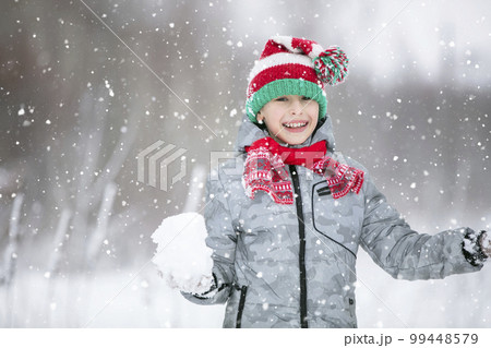 Portrait of a boy in a winter hat. Winter, outside, snow. A child plays with snow. Happy child in winter. 99448579