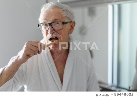 Senior man cleaning his teeth with wooden brush in bathroom, sustainable lifestyle. Senior man cleaning his teeth with wooden brush in bathroom, sustainable lifestyle. 99449002