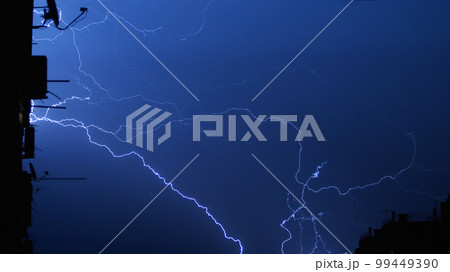 Lightning in the city night sky, bright flashes in the clouds during thunderstorms. Several flashes of lightning at night against the background of a multi-storey building. Lightning in the city night sky, bright flashes in the clouds during thunderstorms. Several flashes of lightning at night against the background of a multi-storey building. 99449390