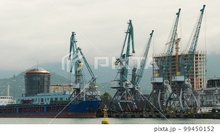 A commercial harbour with harbour cranes. The crane is unloading dry cargo. Close-up. Export and import of dry goods by sea. A commercial harbour with harbour cranes. The crane is unloading dry cargo. Close-up. Export and import of dry goods by sea. 99450152