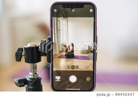 Young woman with little daughter fitness blogger doing exercises and recording video on mobile phone Young woman with little daughter fitness blogger doing exercises and recording video on mobile phone 99450347