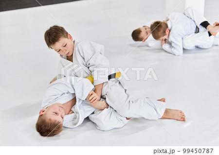 Boys, children in white kimono training, practising judo, jiu-jitsu exercises indoors. Competition. Strength Boys, children in white kimono training, practising judo, jiu-jitsu exercises indoors. Competition. Strength 99450787
