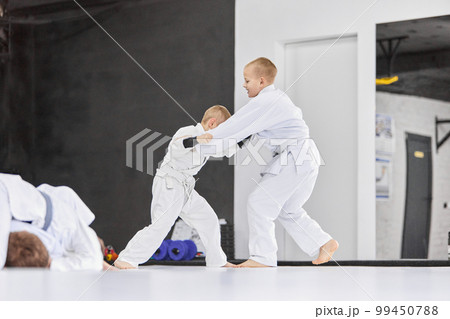 Defense. Boys, children in white kimono training, practising judo, jiu-jitsu exercises indoors. Professional sport athletes Defense. Boys, children in white kimono training, practising judo, jiu-jitsu exercises indoors. Professional sport athletes 99450788