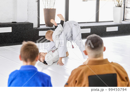 Kids training judo, jiu jitsu, practising exercises in front of coach and pupils. Children learning indoors 99450794