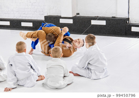 Teacher, professional judo, jiu jitsu coach training kinds, boys, showing exercises. Children learning indoors. Attentive kids 99450796