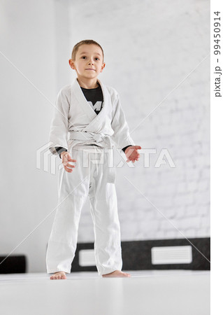 Portrait of little boy, child in white kimono attending sport class, training judo, jiu-jitsu in gym. Sportive active kid Portrait of little boy, child in white kimono attending sport class, training judo, jiu-jitsu in gym. Sportive active kid 99450914