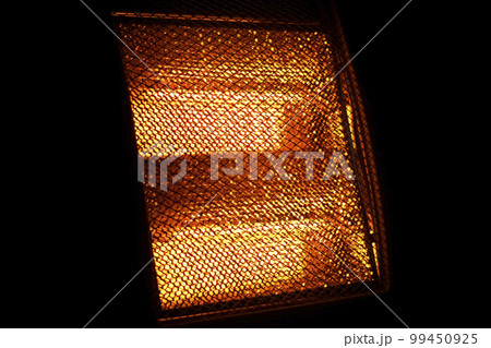 Glowing heating element of hot home electric heater. Orange warm light on black background Glowing heating element of hot home electric heater. Orange warm light on black background 99450925