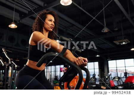 African American woman is losing weight while exercising hard on a bicycle in the gym. 99452438