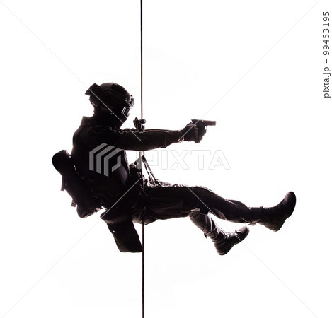 Silhouette of police officer in tactical gear descending from a height, rope exercises with weapons. Tactical rappelling, anti-terror or counter terrorism operation in darkness in rappelling harness Silhouette of police officer in tactical gear descending from a height, rope exercises with weapons. Tactical rappelling, anti-terror or counter terrorism operation in darkness in rappelling harness 99453195