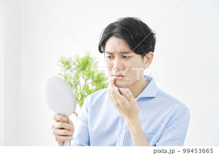 鏡を見て肌荒れに悩む男性 99453665