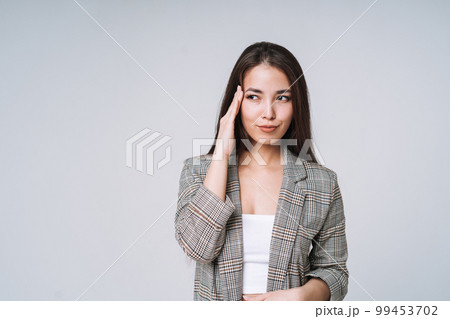 Young unhappy asian business woman in suit and jeans holding her hands on head on grey background 99453702