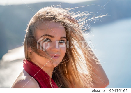 A woman in a red flying dress fluttering in the wind, against the backdrop of the sea. A woman in a red flying dress fluttering in the wind, against the backdrop of the sea. 99456165