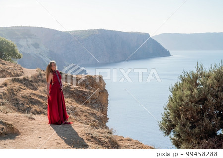 A woman in a red flying dress fluttering in the wind, against the backdrop of the sea. 99458288